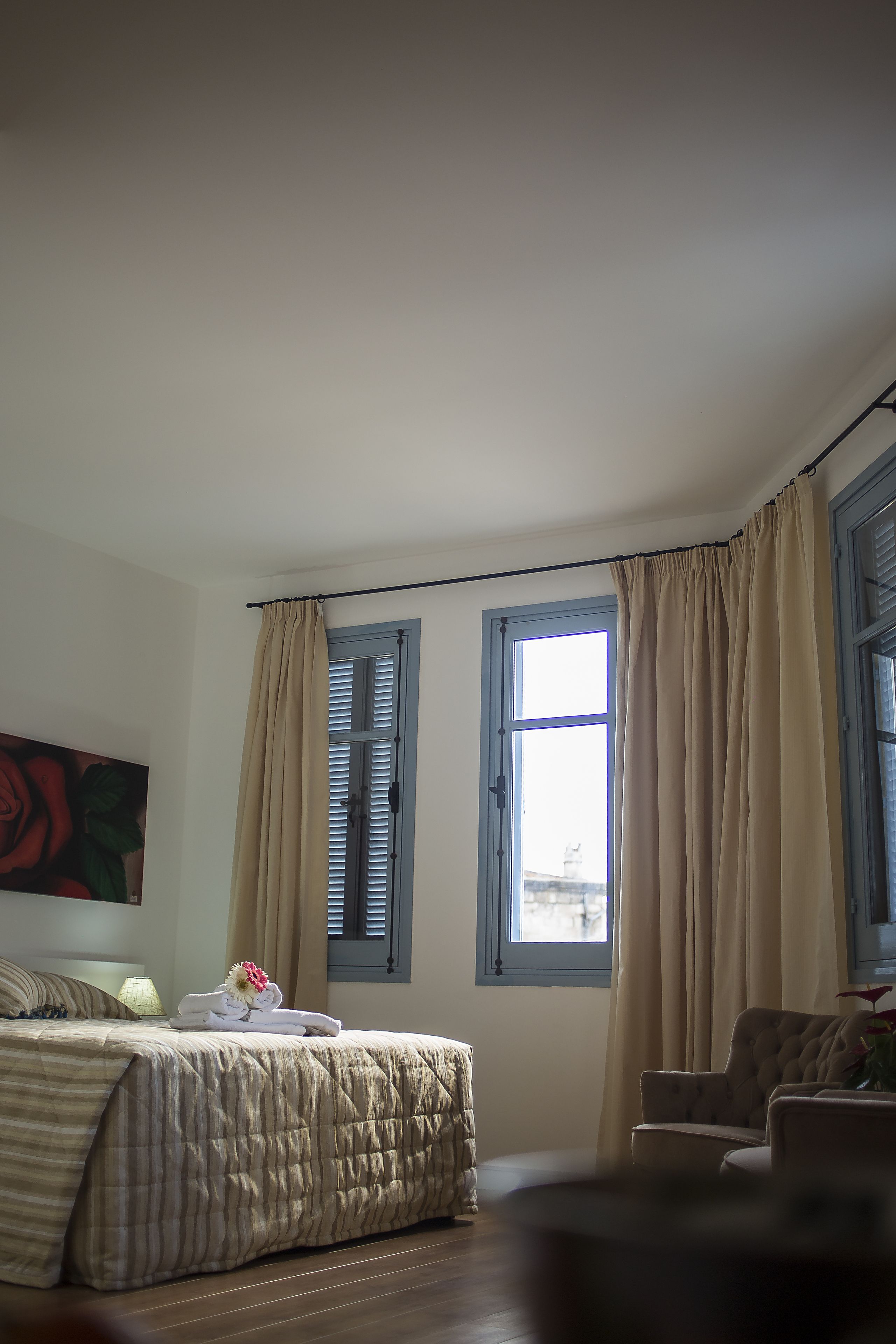 A bedroom with a bed, two windows with curtains, a chair, and a painting on the wall.