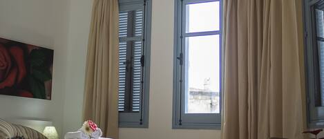 A bedroom with a bed, two windows with curtains, a chair, and a painting on the wall.