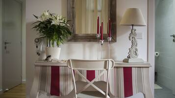A room with a white chair, a mirror, a vase with white flowers, and a lamp.
