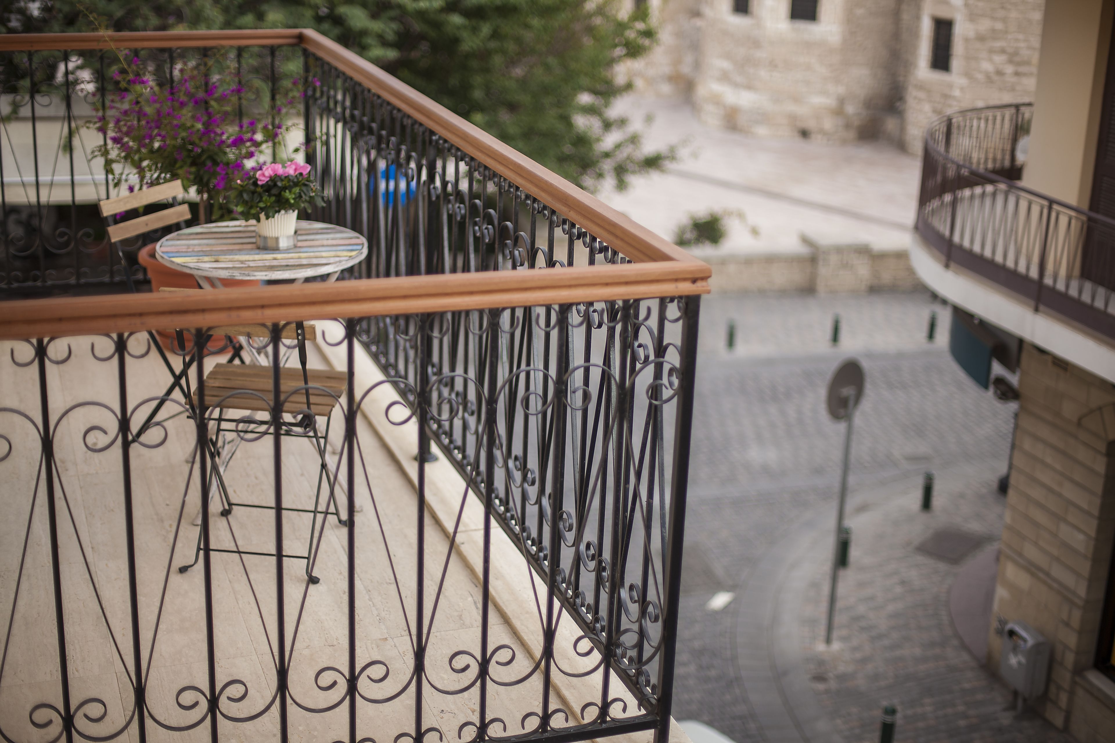 A balcony with a wooden railing, a small round table, and a potted plant with pink flowers.