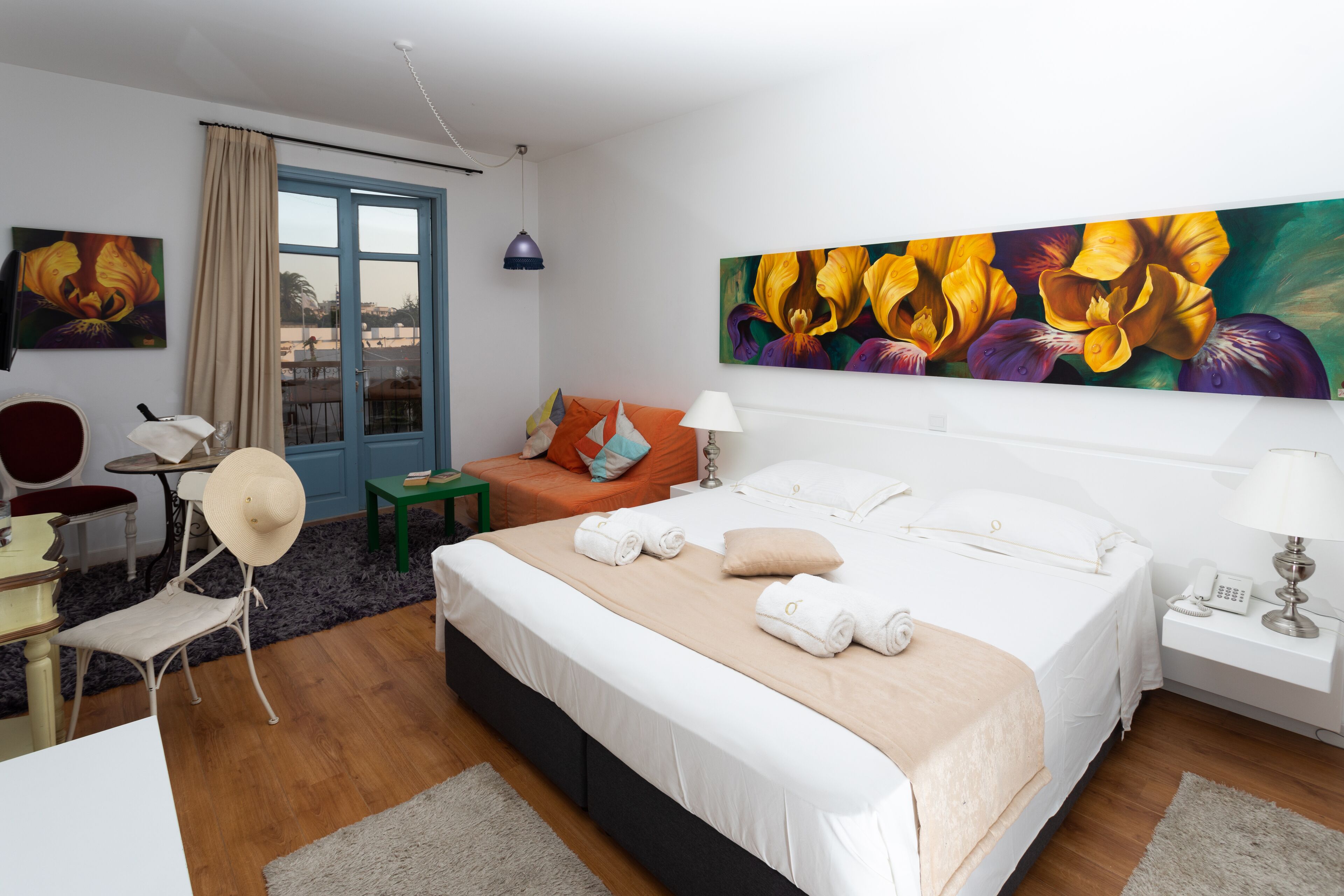 Habitación de hotel con una cama grande, un escritorio con silla, una mesita pequeña, una ventana con cortinas y un cuadro en la pared.