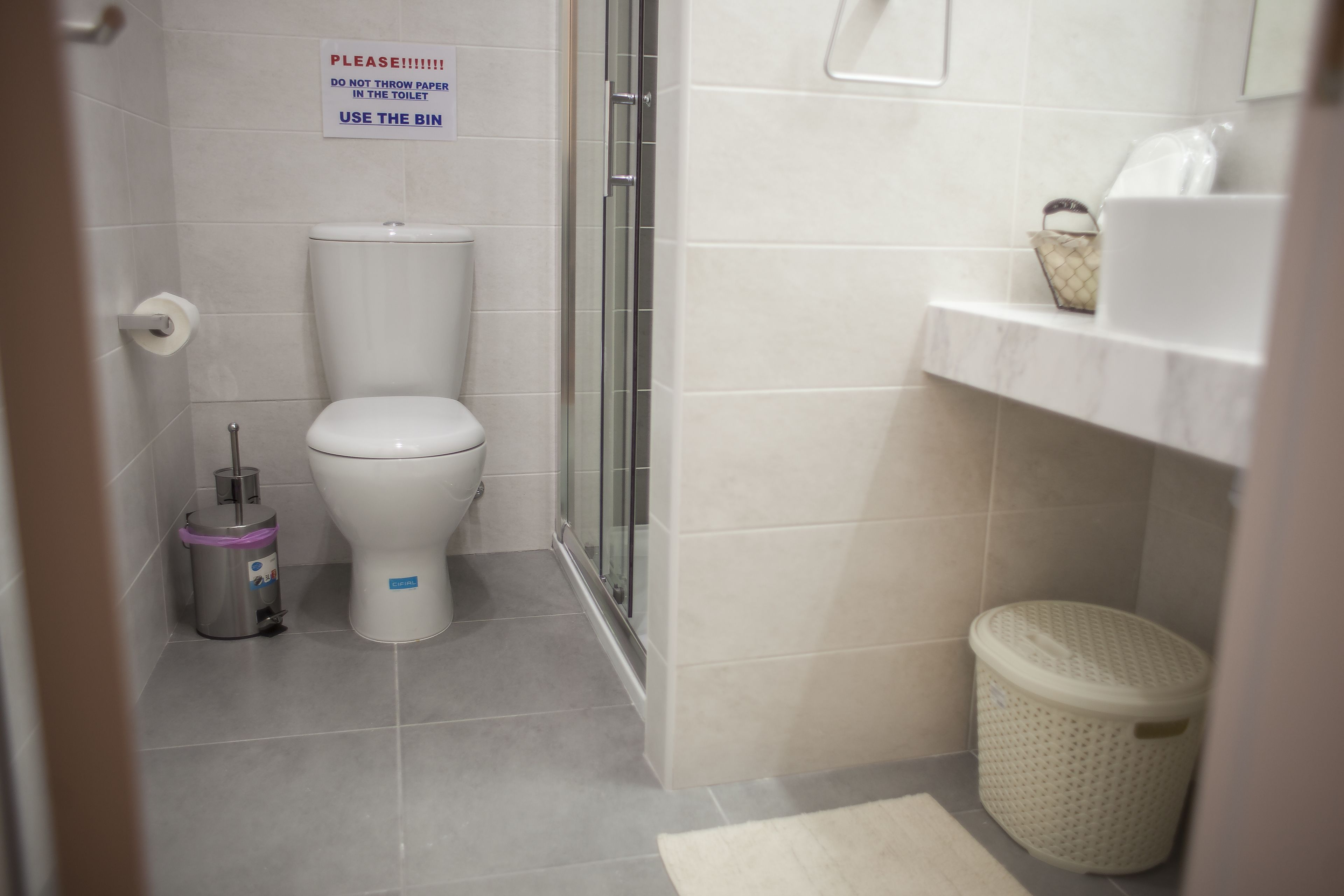 Une salle de bain comprenant des toilettes, une poubelle et un espace douche.