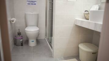 A bathroom with a toilet, a trash bin, and a shower area.
