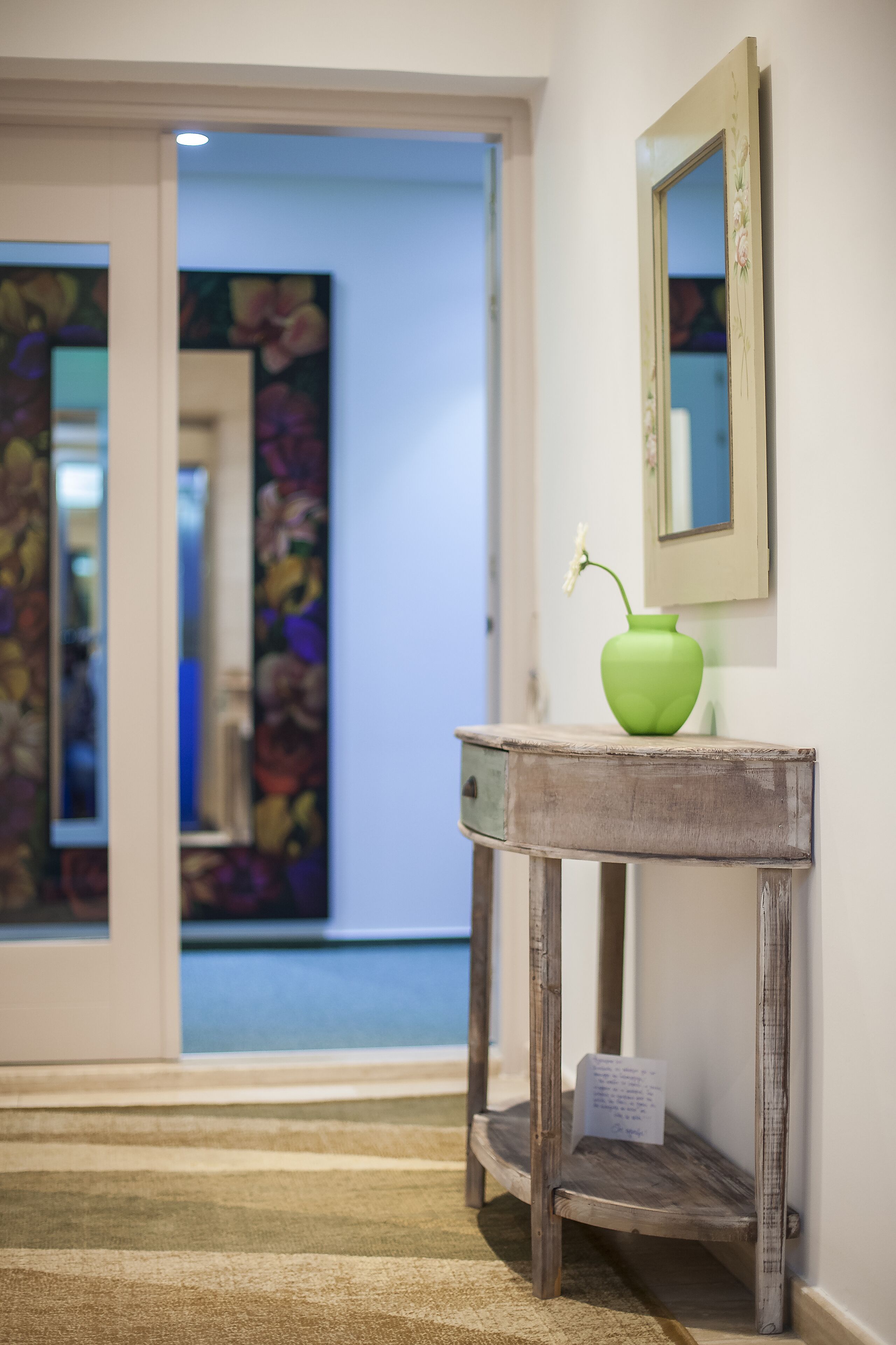 A hallway with a wooden console table, a green vase with a flower, and a mirror on the wall.