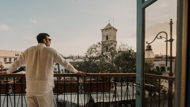 A man standing on a balcony overlooking a cityscape with a prominent tower. - Operetta House (Larnaca)
