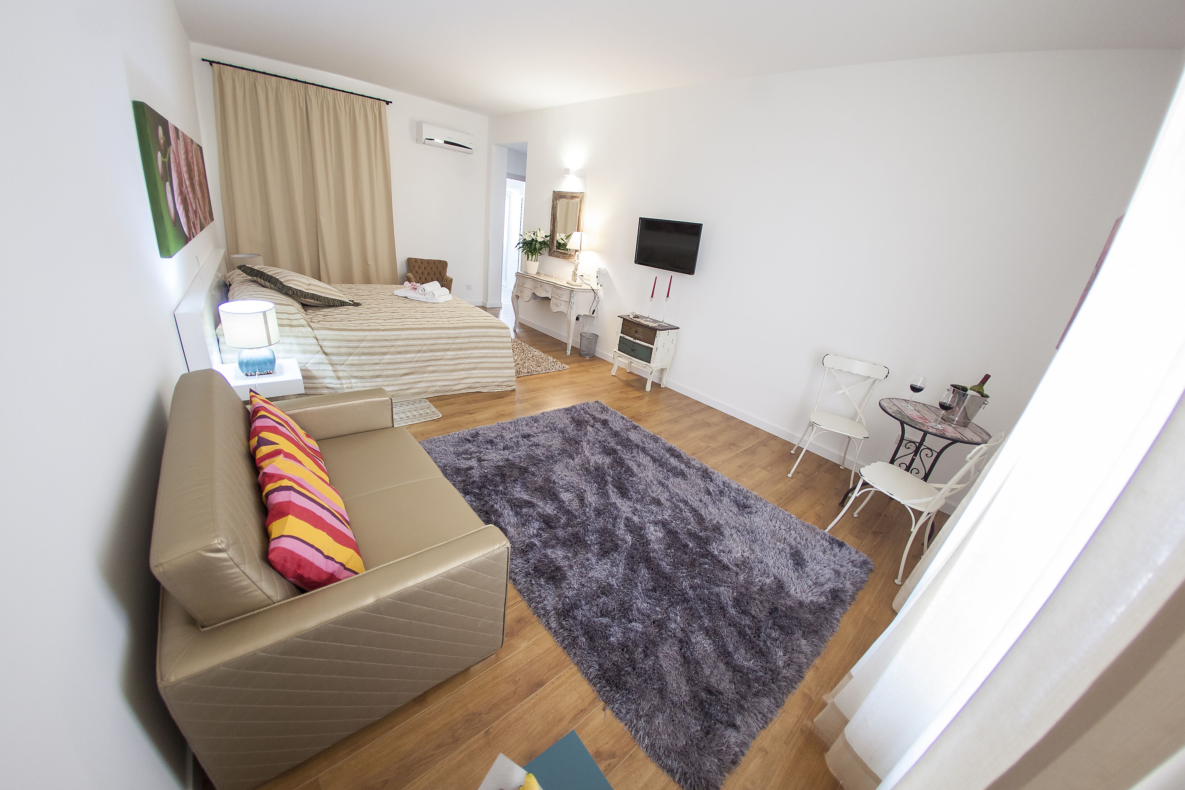 A modern hotel room with a bed, a sofa, a desk, and a TV.