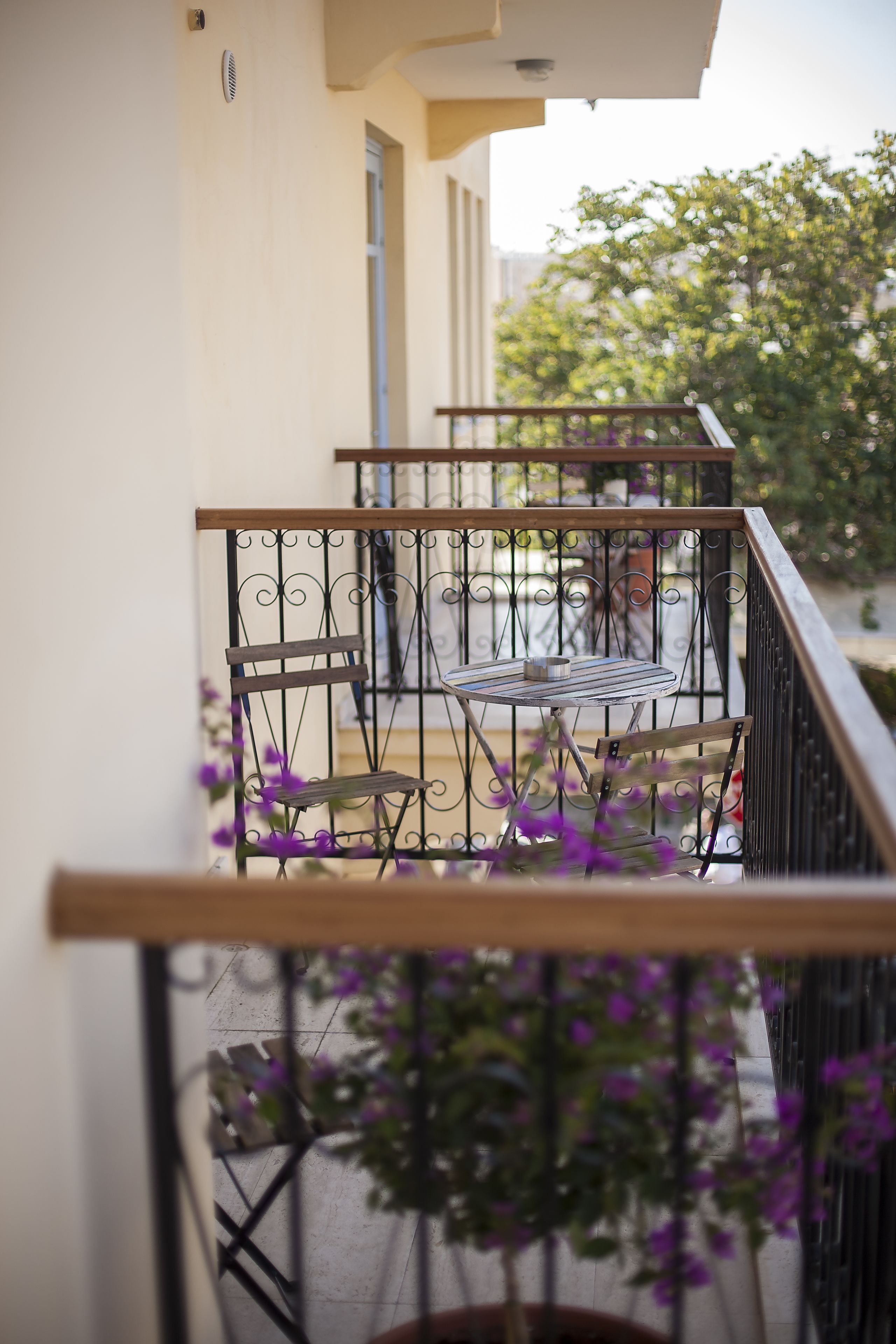 Un balcon doté d’une rambarde en métal, d’un banc en bois et d’un pot de fleurs contenant des plantes aux fleurs violettes.