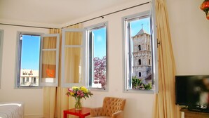 A room with a bed, a chair, a small table with flowers, and a TV. - Operetta House (Larnaca)