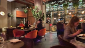 A restaurant with tables and chairs, a bar area with bottles, and a large pillar with greenery. - Boutique Hotel The Roosevelt (Middelburg)