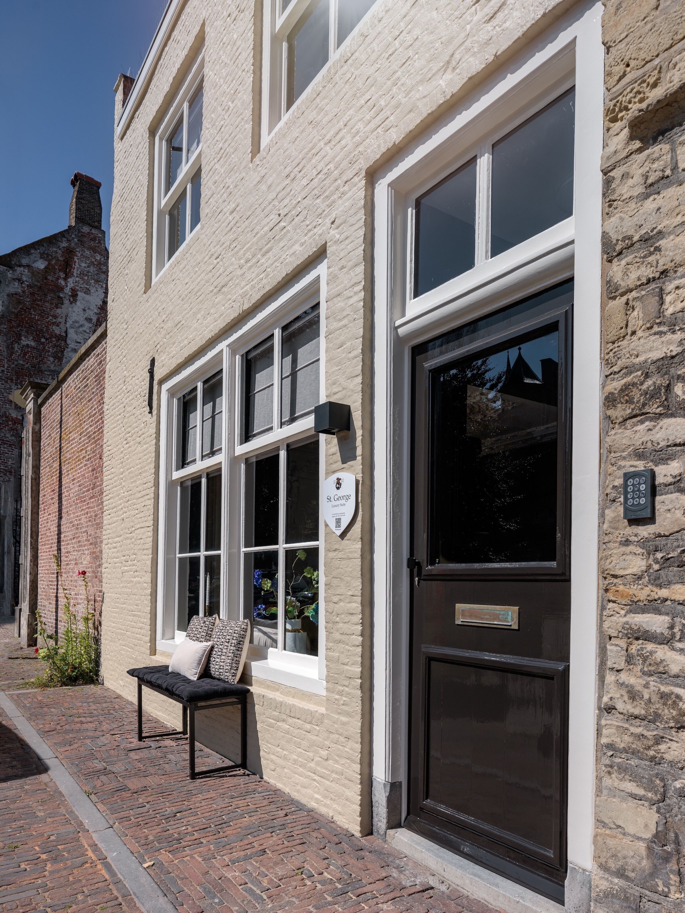 A building with a stone facade, large windows, a black door, and a bench outside.