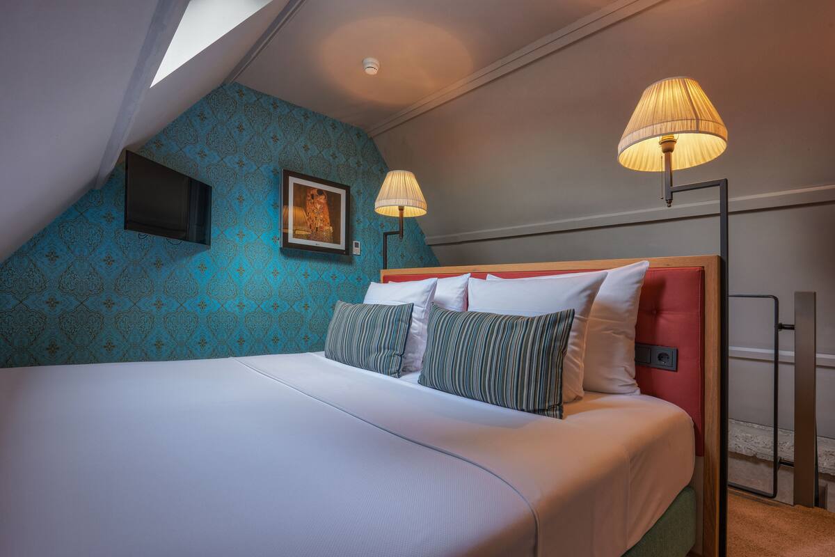 Une chambre à coucher avec un grand lit, deux lampes de chevet, un tableau au mur et une tête de lit rouge.