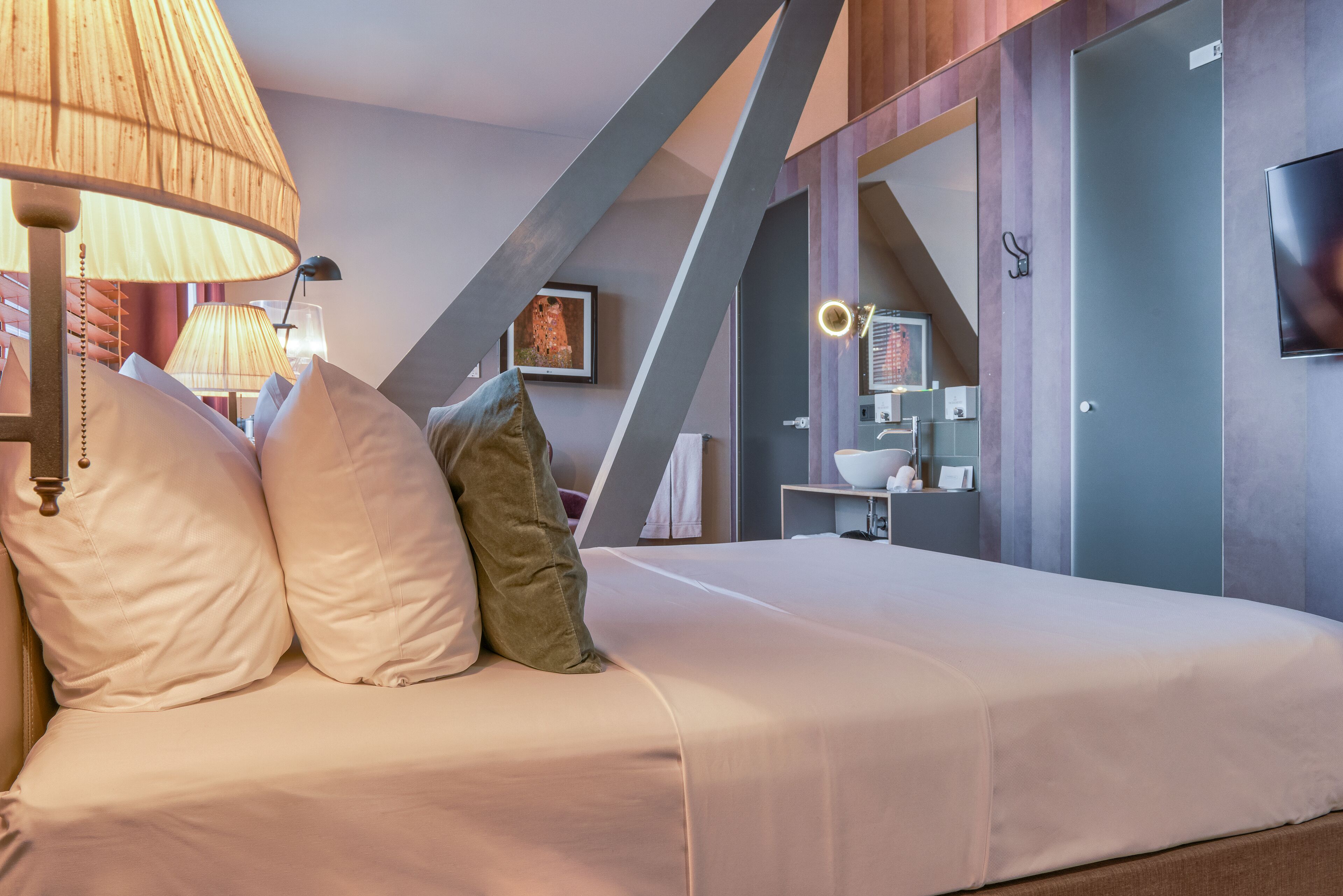 Une chambre d’hôtel moderne équipée d’un lit, d’oreillers, d’une lampe, d’un miroir et d’un téléviseur.