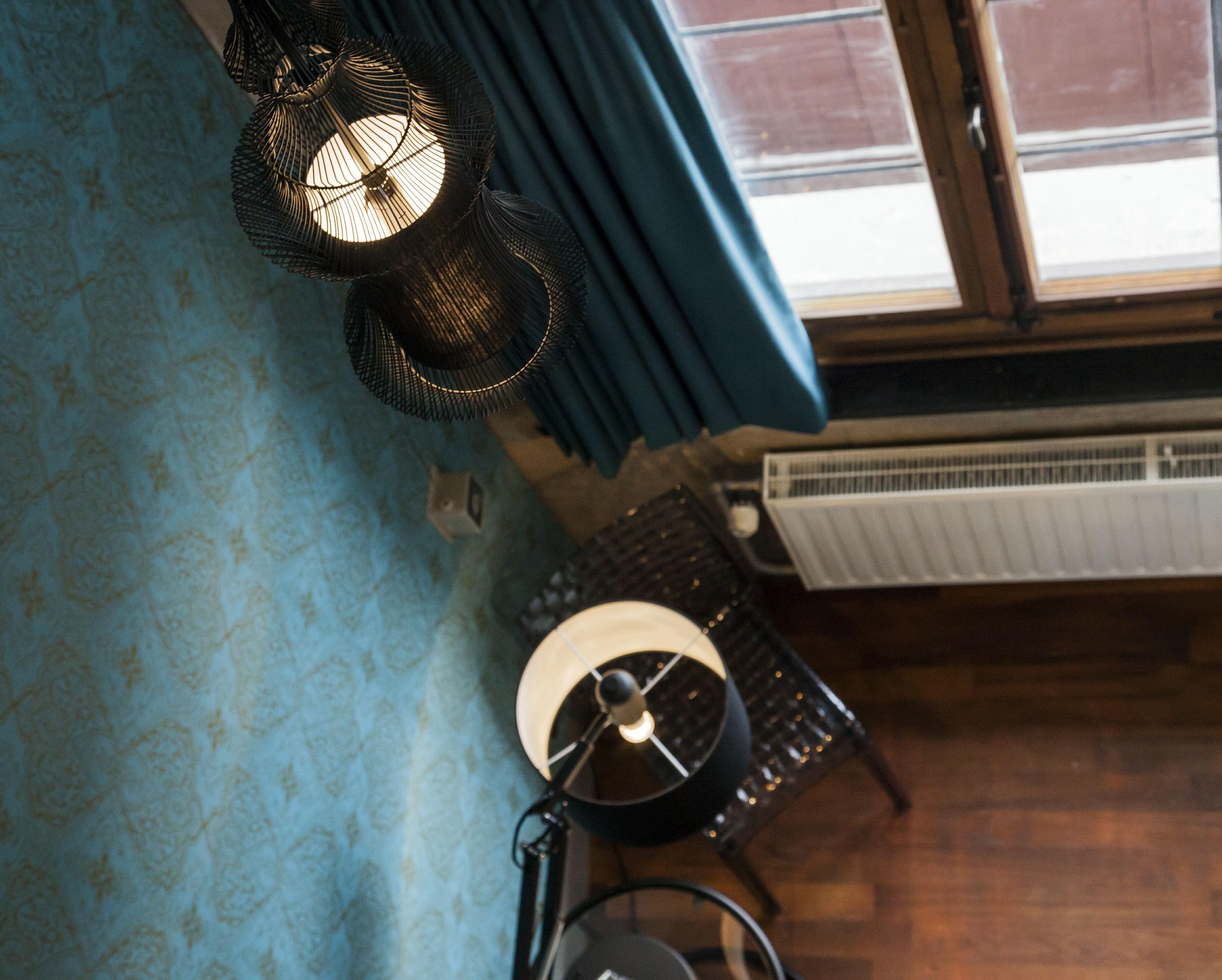 A room with a patterned blue wall, a black lamp, a radiator, and a window with curtains.