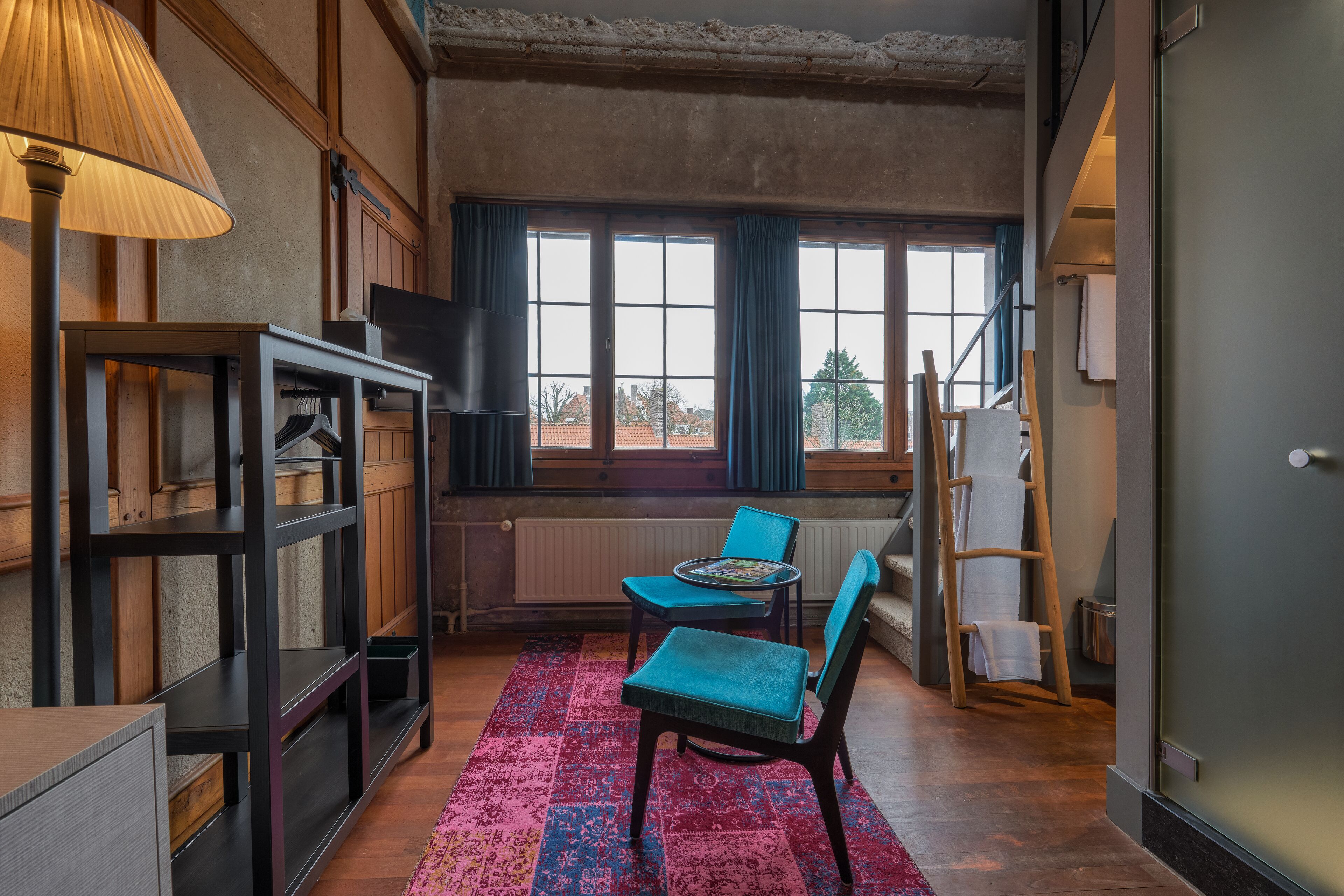 A room with a large window, a table with chairs, a lamp, and a ladder.