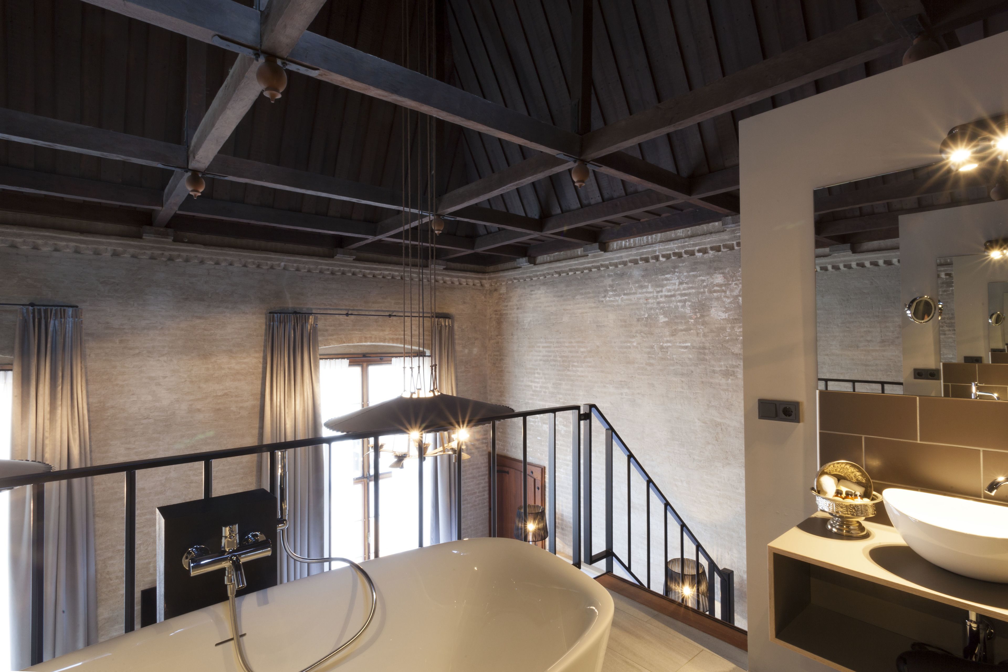 Un bagno moderno con una vasca freestanding, un mobile lavabo con un ampio specchio e una scala che conduce a un piano superiore.