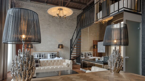 A spacious living area with a high ceiling, a staircase, and a modern chandelier. - Boutique Hotel The Roosevelt (Middelburg)