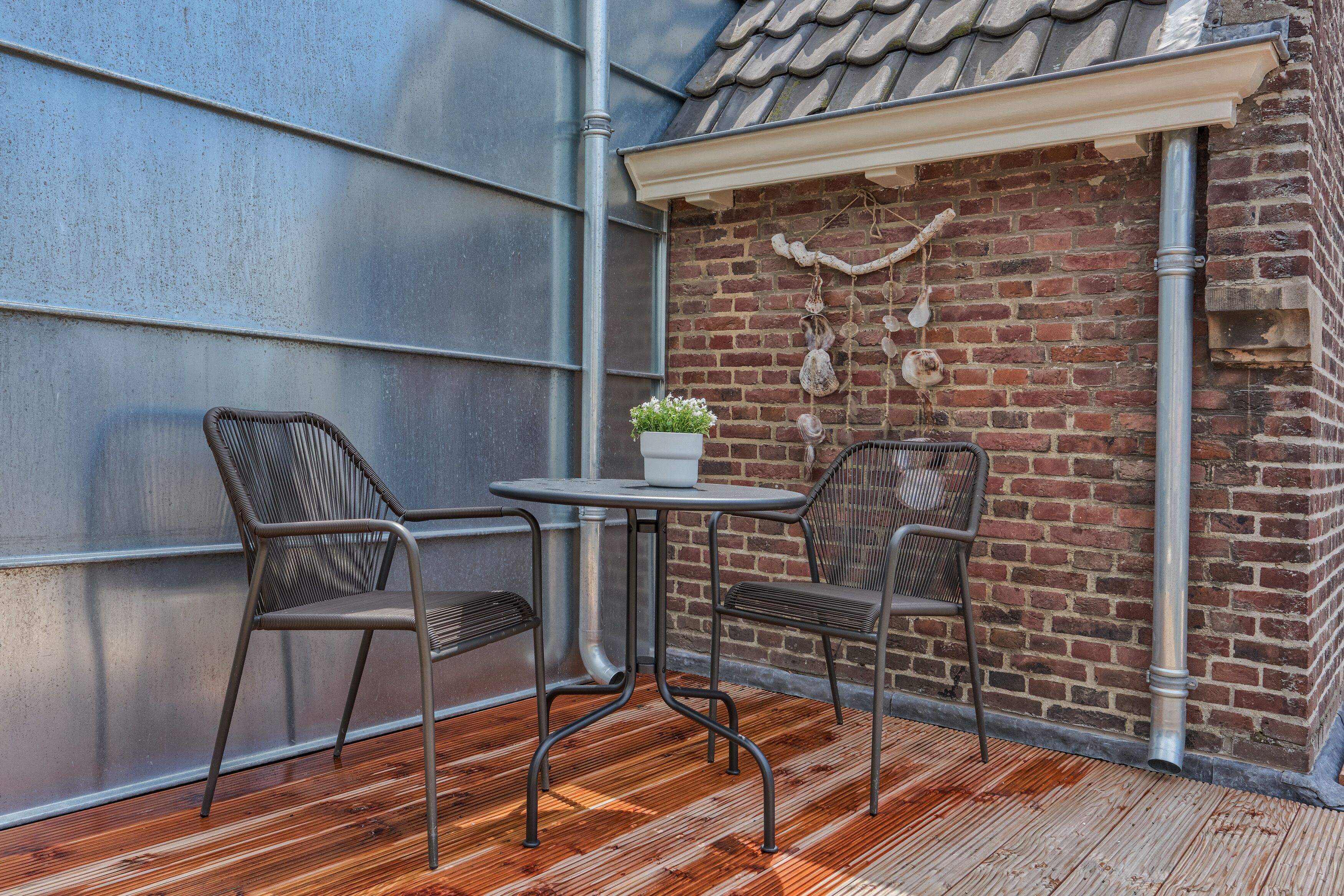 A small outdoor seating area with two chairs and a table, a potted plant, and a brick wall with decorative elements.