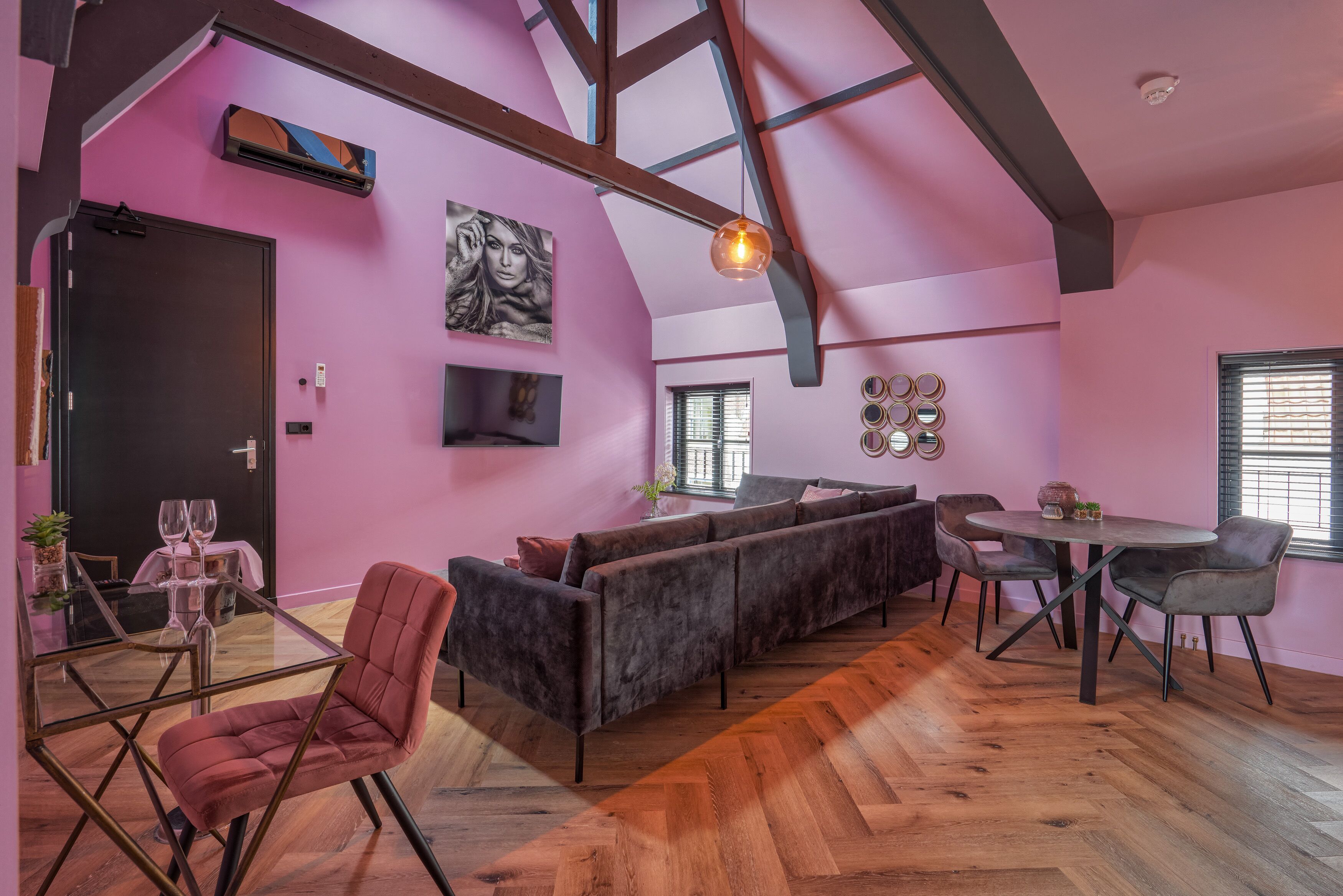 A modern interior with a pink wall, a wooden ceiling, a sofa, a dining table, and chairs.