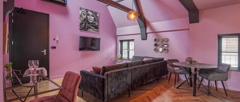 A modern interior with a pink wall, a wooden ceiling, a sofa, a dining table, and chairs.