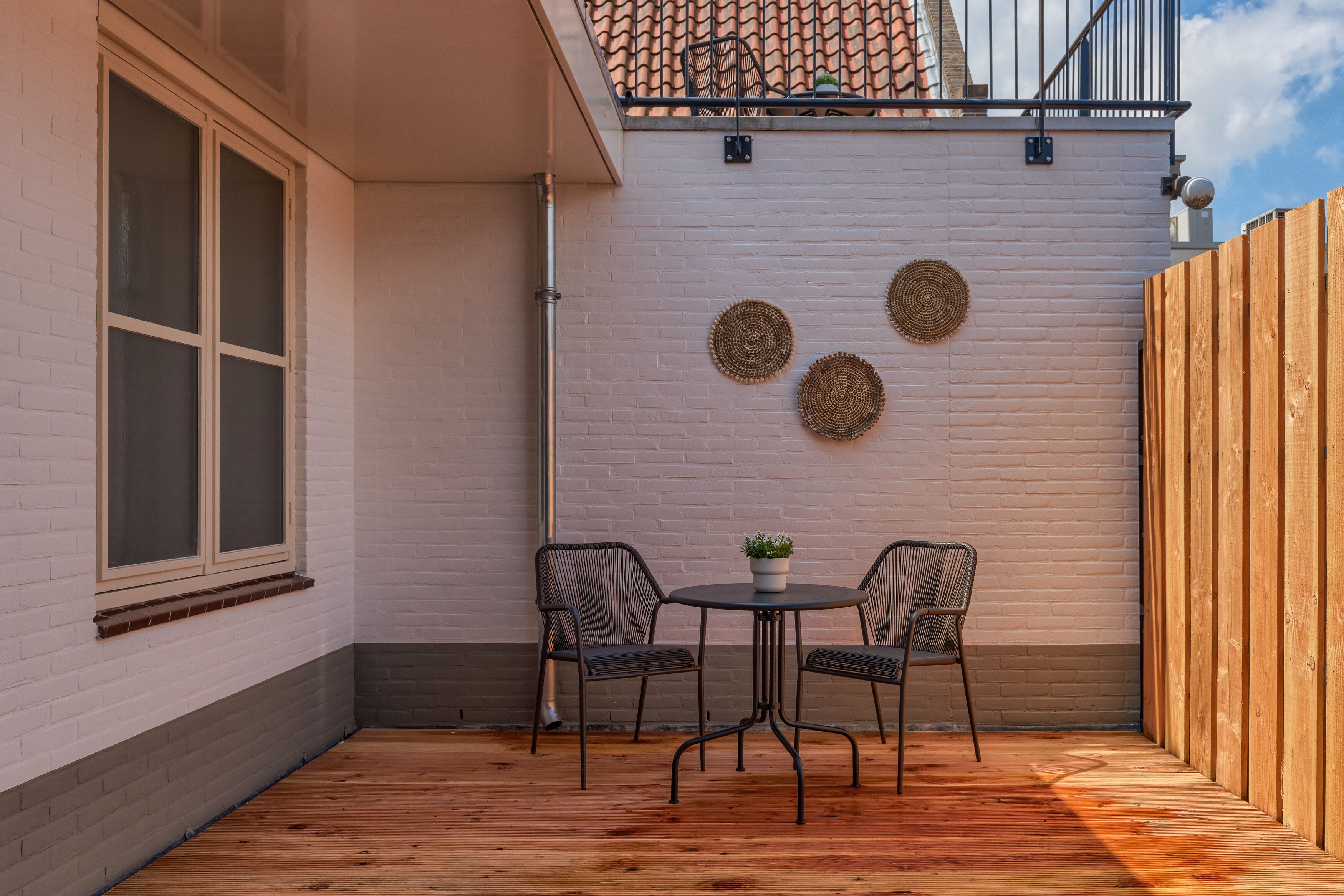 A patio with two chairs and a table, a white brick wall, and a wooden fence.