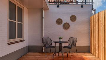 A patio with two chairs and a table, a white brick wall, and a wooden fence.