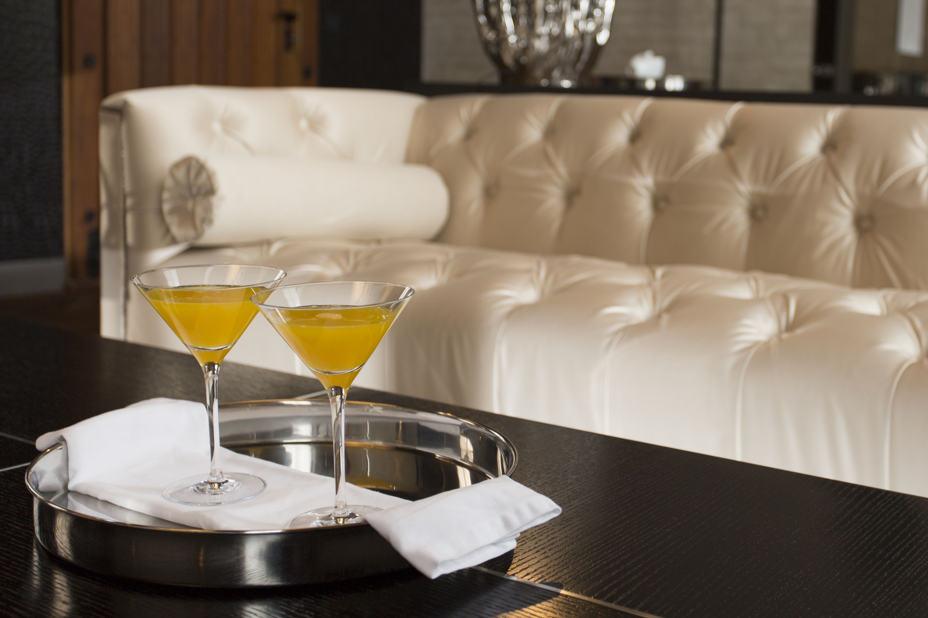 A dining table with two martini glasses on a tray, a white napkin, and a white cushioned sofa in the background.