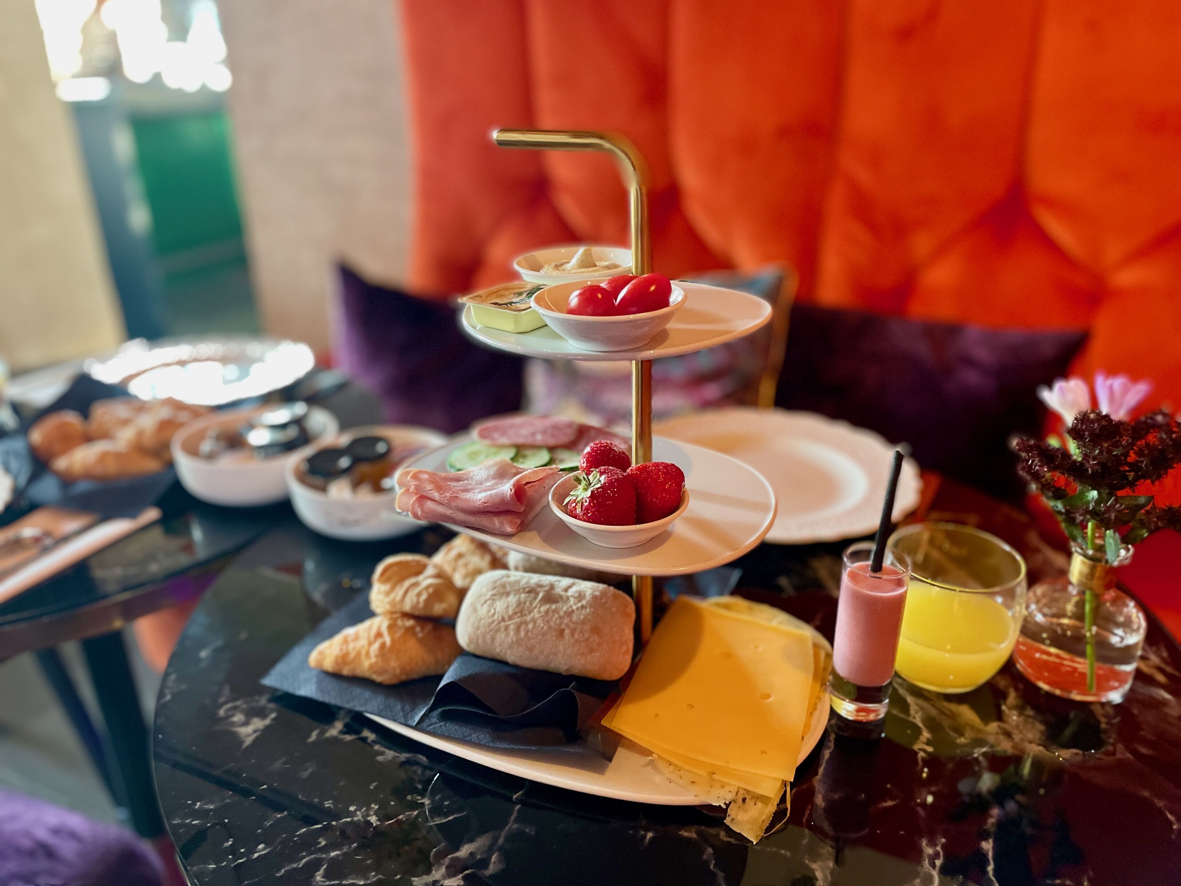 A three-tiered dessert stand with strawberries and a bottle of juice on a marble table.