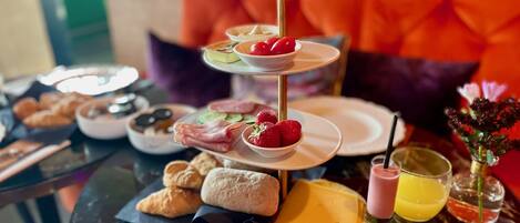 A three-tiered dessert stand with strawberries and a bottle of juice on a marble table.
