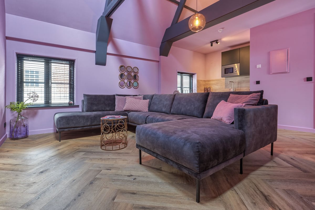 Un salon moderne avec un canapé d’angle, une table basse ronde et un parquet en bois à motifs chevrons.