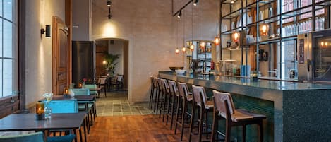 A restaurant with wooden floors, bar seating, and a kitchen area with shelves of bottles.