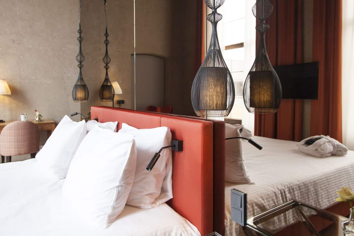Une chambre d’hôtel avec un grand lit, un plus petit lit, un bureau et une chaise. Deux luminaires sont suspendus au-dessus des lits.