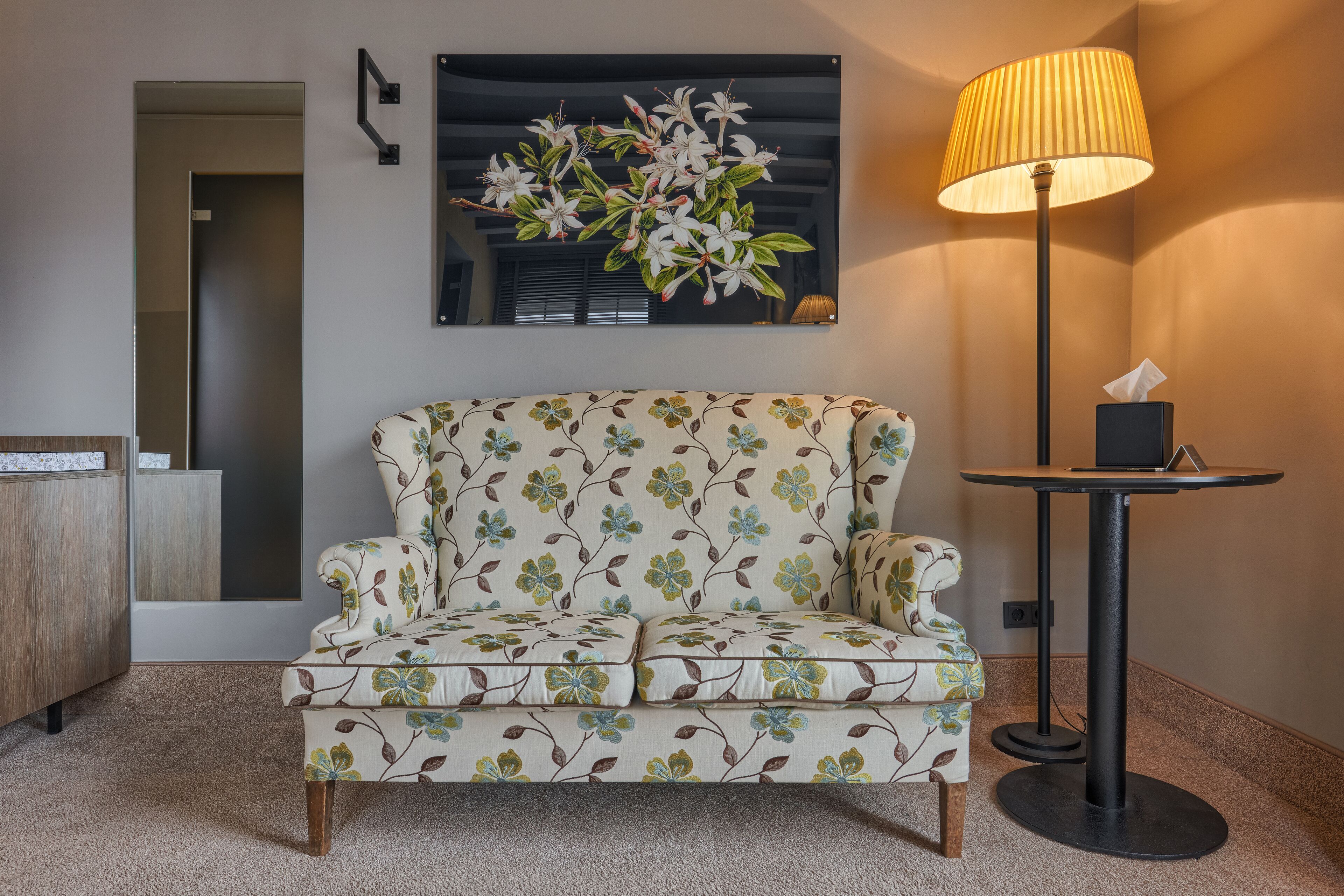 A floral-patterned sofa, a standing lamp, and a framed floral artwork on the wall.
