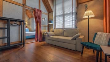 Una habitación acogedora con sofá, sillón, mesa, lámpara y cama con ventana y cortinas.