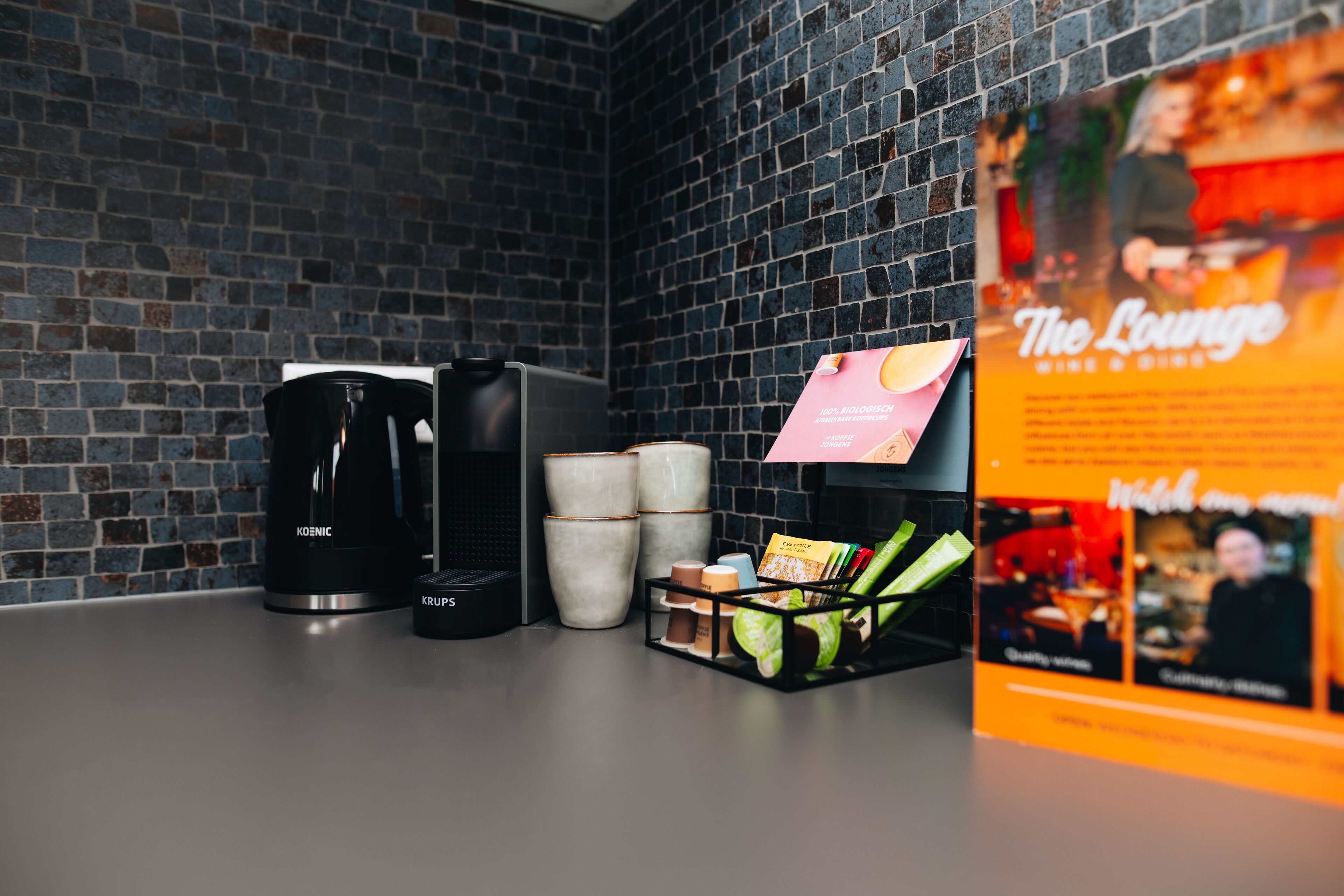 A coffee station with a Krups coffee maker, a Keurig, and several mugs. There is a sign for "The Lounge" with a menu.