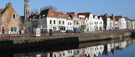 A canal with buildings reflecting on the water, a tower, and a clear sky.