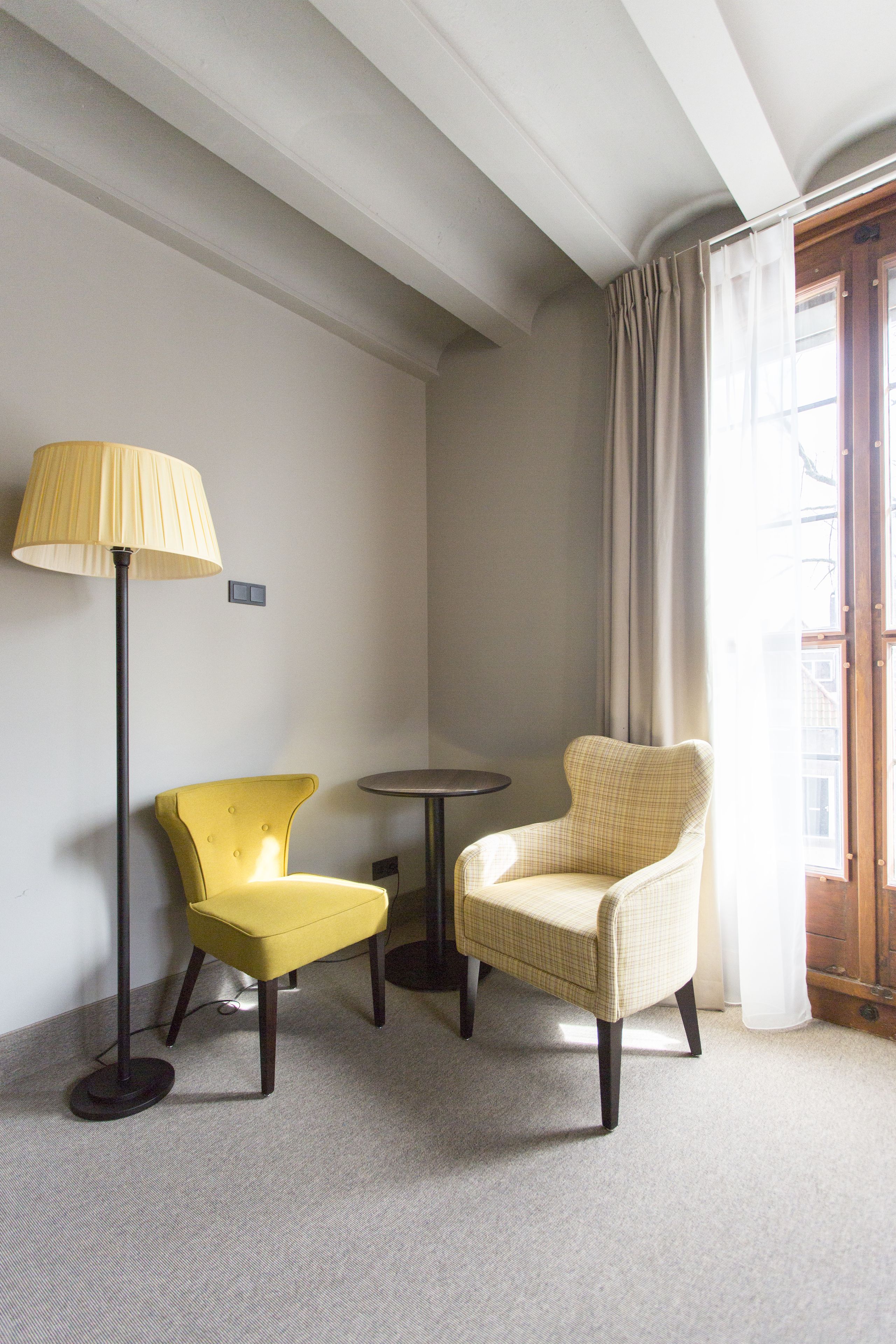 A room with a yellow armchair, a beige armchair, a floor lamp, and a small round table.