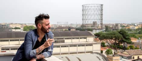 A man leaning on a balcony railing with a cityscape in the background.