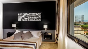 Habitación de hotel con una cama grande, dos lámparas de noche, un cuadro del Coliseo y vistas a una obra en construcción por la ventana.