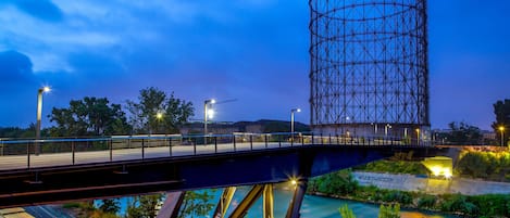 Un puente con estructura metálica, un río abajo y un edificio con grafitis al fondo.