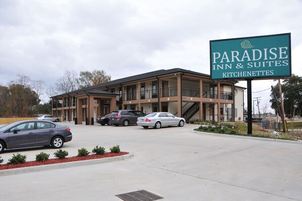 A building with a sign reading "Paradise Inn & Suites Kitchens." It has a modern design with multiple floors and a covered parking area.