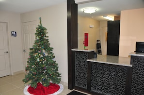 A Christmas tree in a hotel lobby with a reception desk and a door marked "Men's Restroom".