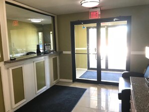 A reception area with a counter, a mirror, a door with an exit sign, and a carpeted floor.