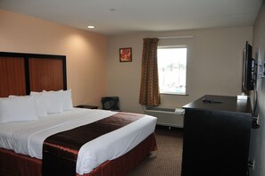 A hotel room with a large bed, a desk, a television, and a window with curtains.