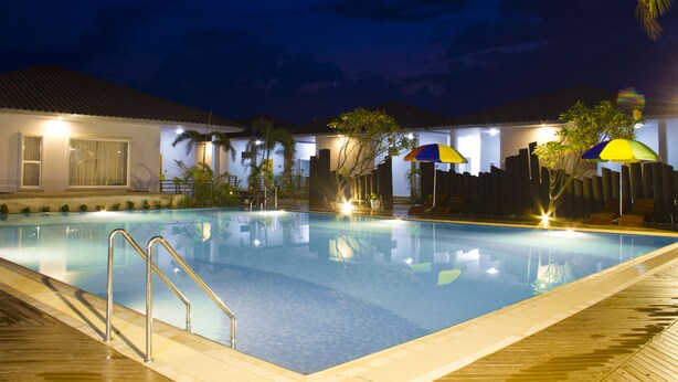 A swimming pool with a wooden deck, surrounded by umbrellas and palm trees, under a night sky. - Triumph Hotel (Mandalay)