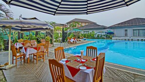 A poolside dining area with tables and chairs, a pool, and a covered seating area. - Triumph Hotel (Mandalay)