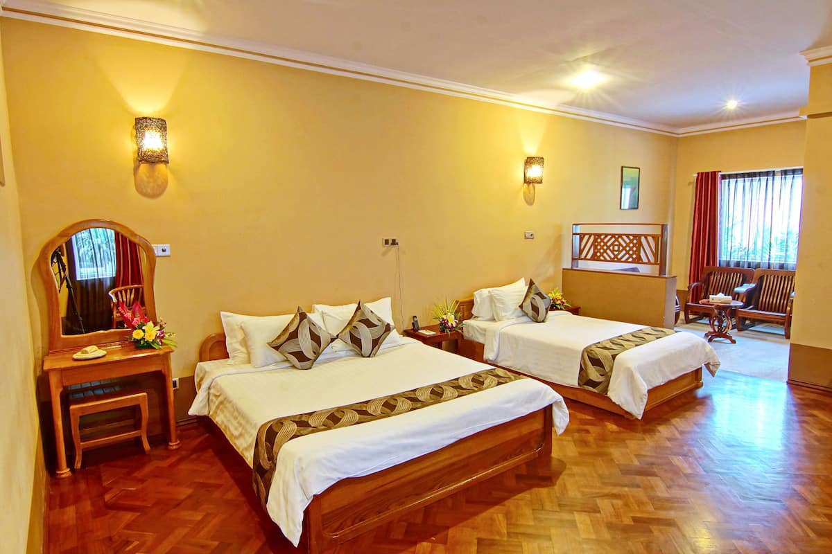 Habitación de hotel con dos camas, suelo de madera, un escritorio con espejo y una silla.
