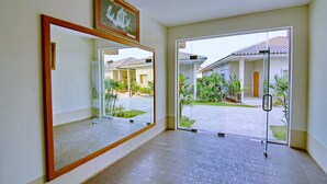 A spacious hallway with a large mirror, a framed picture, and a view of a courtyard with plants and a building. - Triumph Hotel (Mandalay)