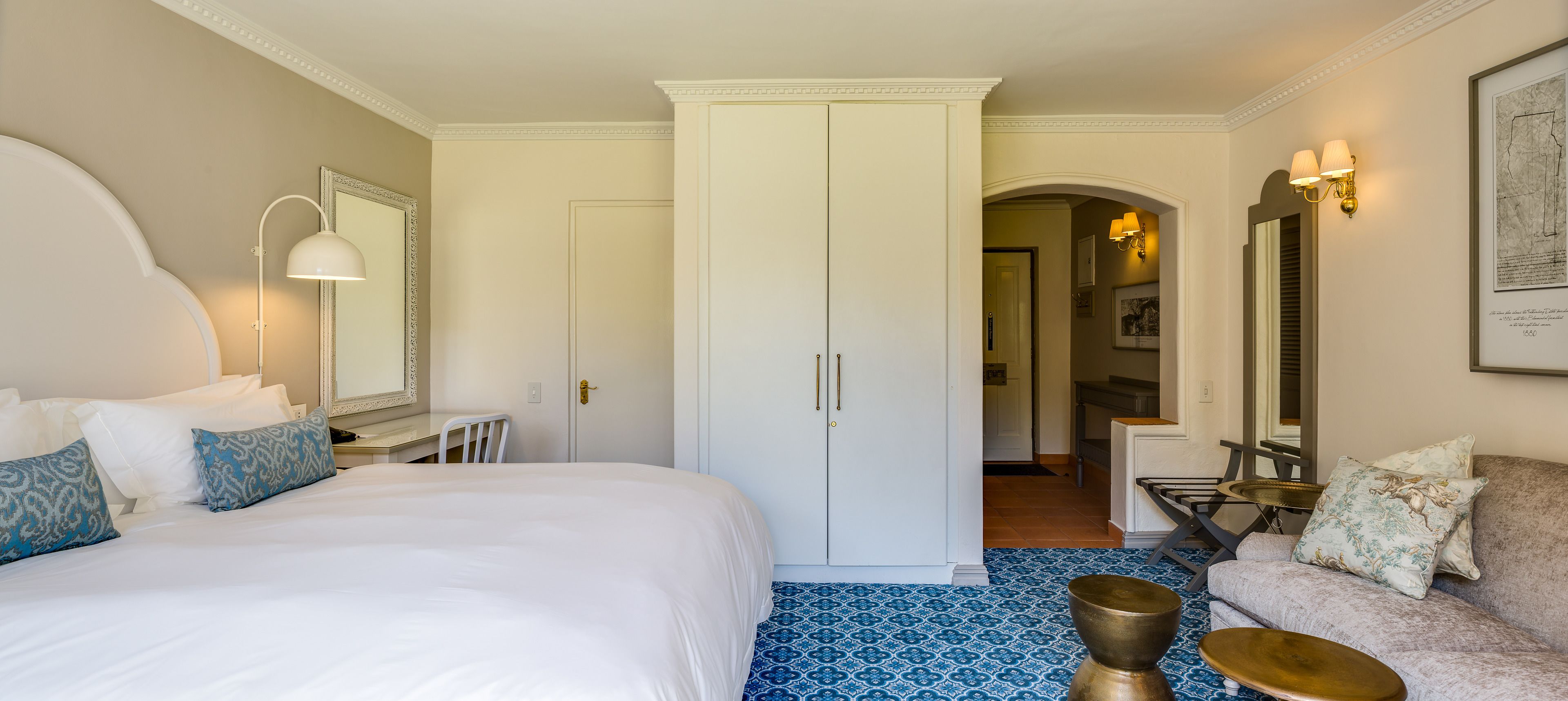 A hotel room with a large bed, a desk, a wardrobe, and a seating area with a sofa and armchairs.