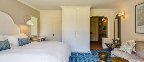 A hotel room with a large bed, a desk, a wardrobe, and a seating area with a sofa and armchairs.