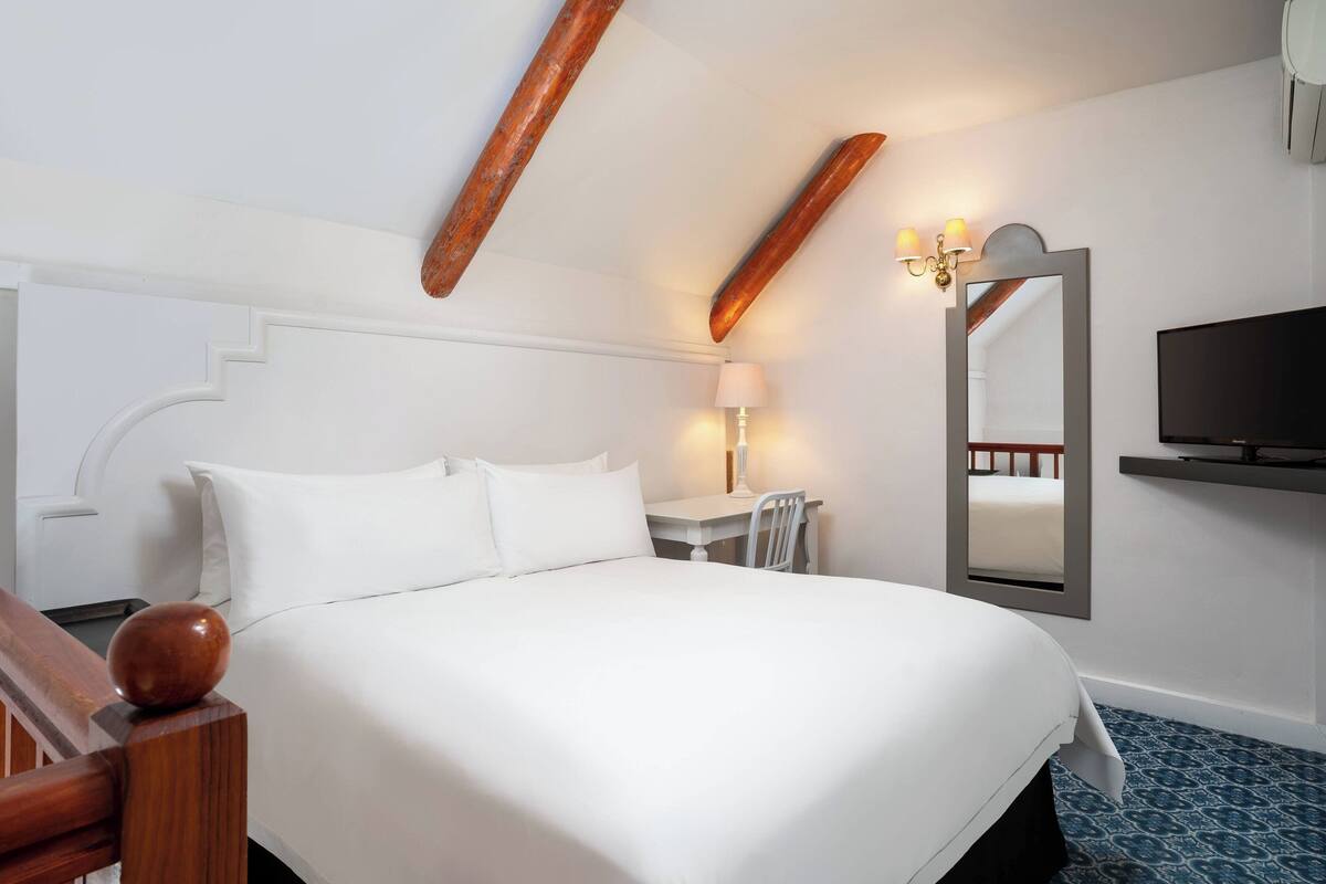 Una camera d'albergo con un letto grande, una scrivania, una sedia, una televisione e uno specchio.